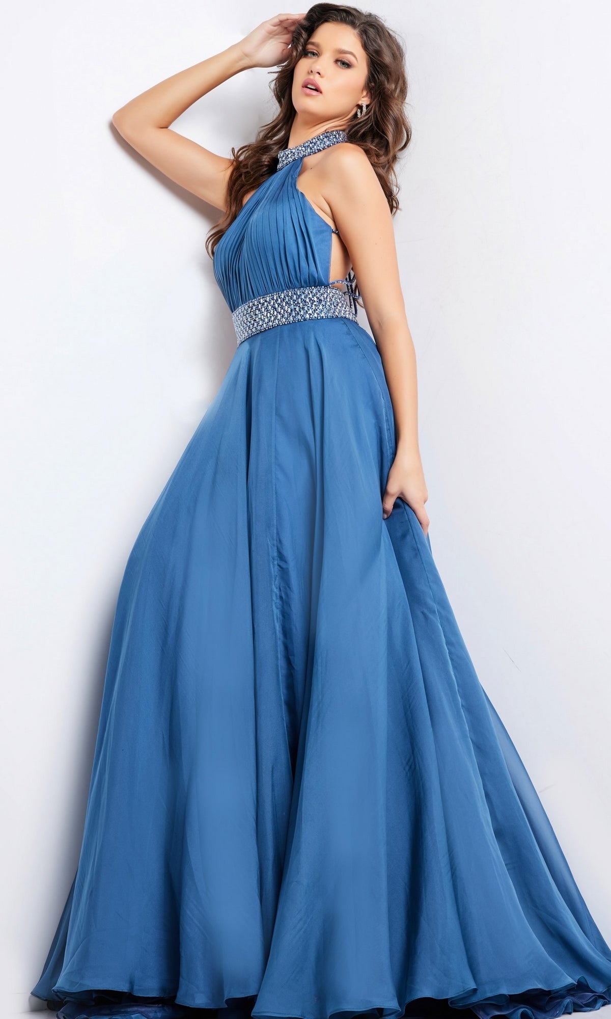 Woman wearing Long Prom Dress 36749 by Jovani, a sleeveless blue A-line gown with silver embellishments at the collar and waist, standing against a plain white background.